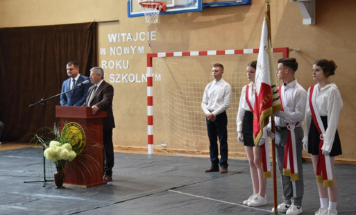 Uczniowie ze stojący ze sztandarem szkoły na uroczystym apelu w trakcie przemowy starszego mężczyzny