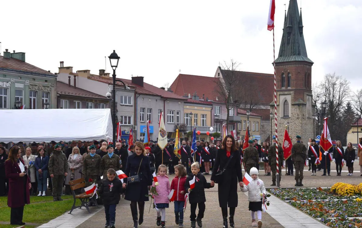grupa os&oacute;b dorosłych i&nbsp;dzieci idące za ręke, niekt&oacute;re trzymają małe flagi biało czerwone
